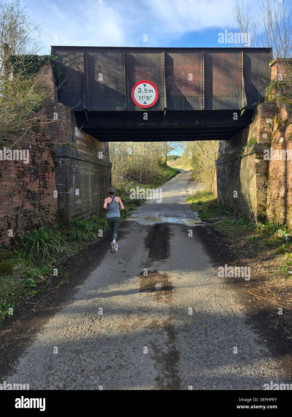 Un coureur passe sous un pont de chemin de fer bas sur une voie de campagne près de Powerstock, une partie de l'ancien chemin de fer Bridport, Dorset, Angleterre, Royaume-Uni - Image de stock capturée avec un smartphone