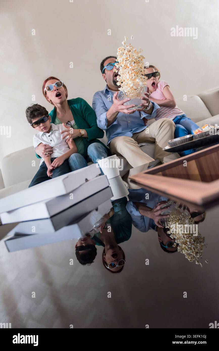 Famille moderne du moyen-Orient regardant un film ensemble à la maison avec pop-corn volant dans le salon surprise Banque D'Images