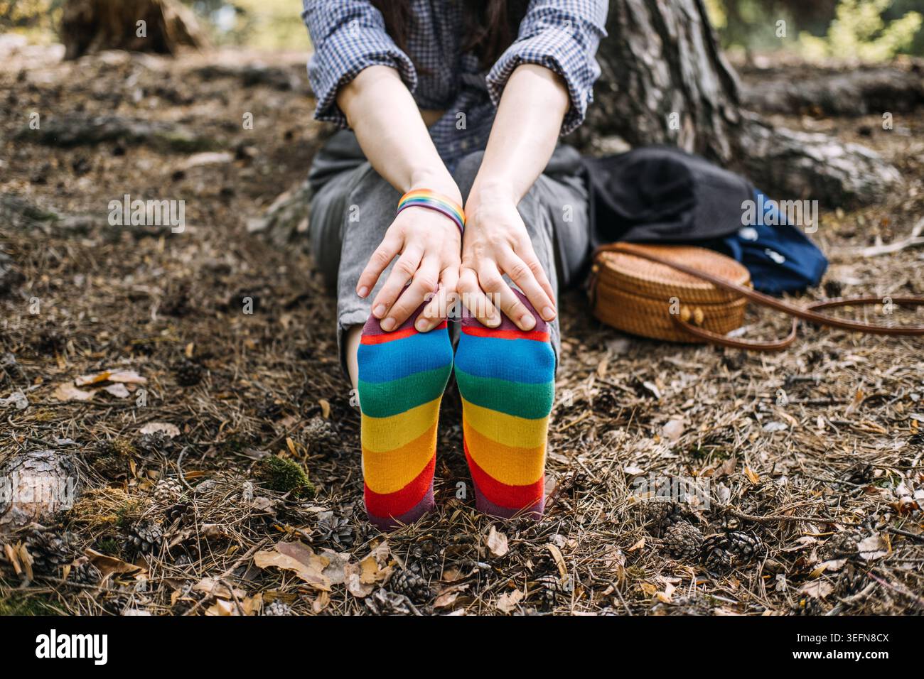 La personne est assise sur le sol de la forêt portant des chaussettes arc-en-ciel avec les pieds pointés vers la caméra. Représentation LGBTQ, vie queer authentique, personne non binaire Banque D'Images