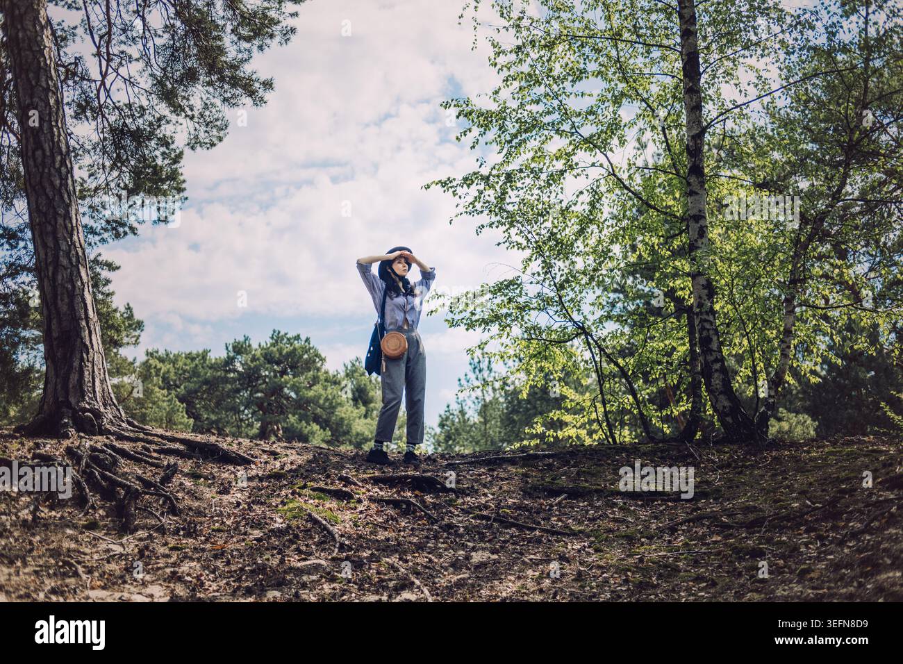 Femme se tient sur la colline de la forêt protégeant les yeux avec les mains tout en regardant le paysage. Mode de vie détox numérique, reconnexion avec l'âme, baignade de forêt Banque D'Images