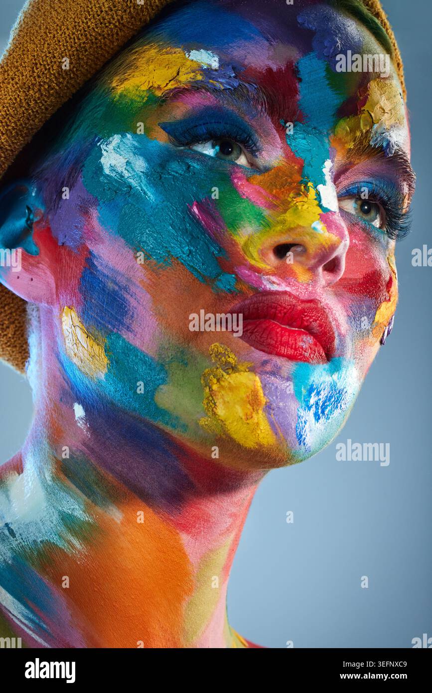 Visage, peinture et femme en studio avec créativité, beauté ou expression de soi sur fond bleu. Coloré, sérieux et personne avec des cosmétiques artistiques Banque D'Images