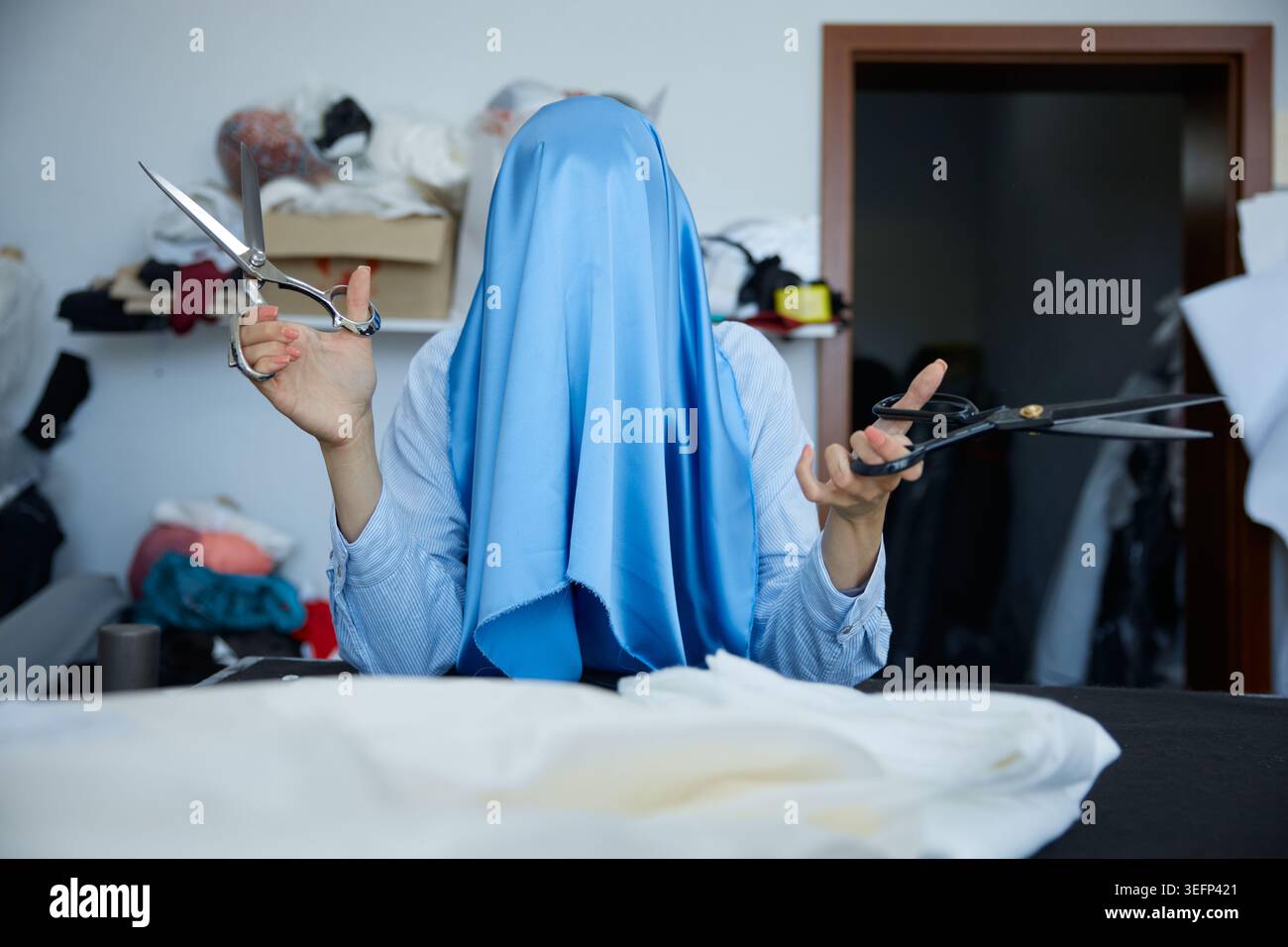 Individuel vêtu de ciseaux bleus tenant sur des matériaux textiles dans le studio Banque D'Images