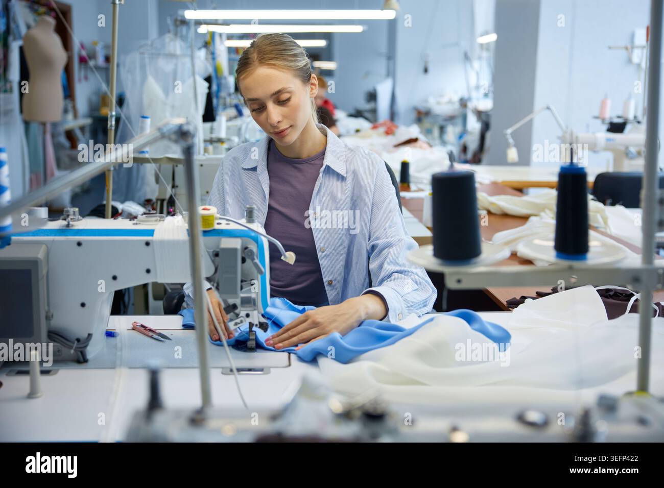 Jeune artisan se concentrant sur des points précis dans un cadre d'atelier moderne Banque D'Images