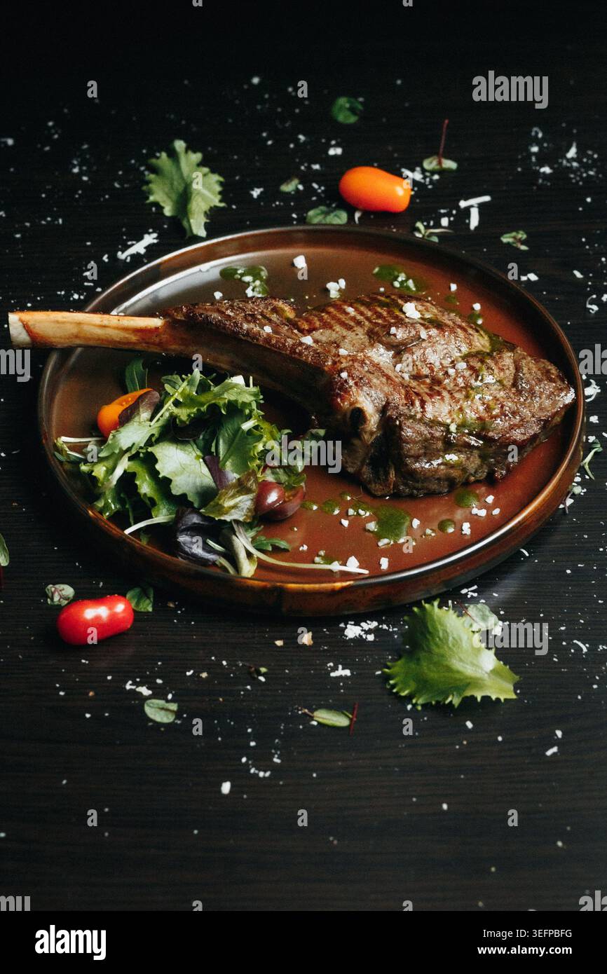 Côtelette d'agneau grésillante avec des légumes verts et des tomates sur une surface en bois foncé Banque D'Images