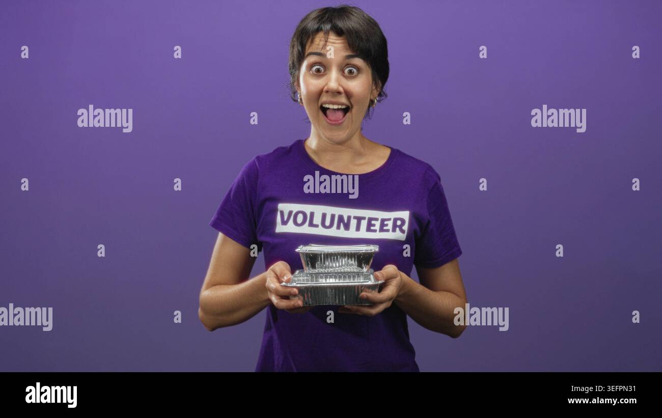 Femme bénévole dans une chemise violette tenant des contenants de nourriture en aluminium avec les mains et offrant des repas, bouche ouverte dans surprise, studio ; service communautaire exci Banque D'Images