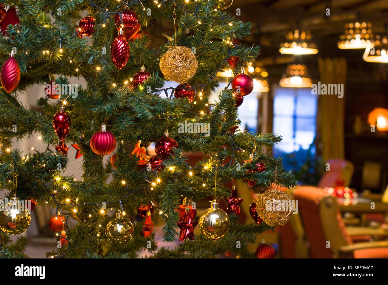 Sapin de Noël décoré avec lumières brillantes, boules dorées et rouges en gros plan. Intérieur de chambre floue de vacances festives sur le fond, Tyrol, Autriche Banque D'Images