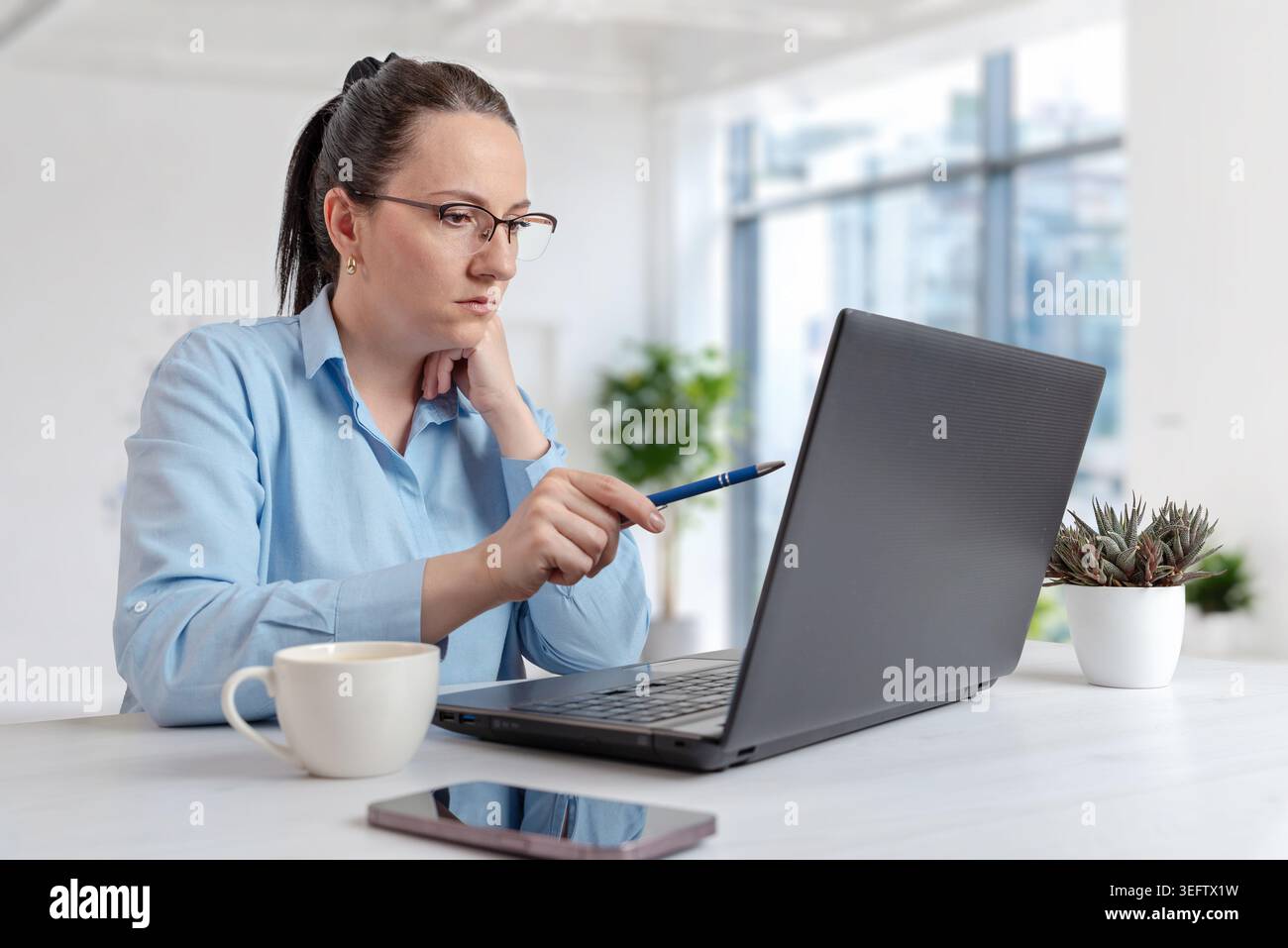 Femme professionnelle concentrée pointant le stylo à l'écran d'ordinateur portable pendant la réunion en ligne ou la session d'analyse d'affaires dans l'environnement de bureau moderne Banque D'Images