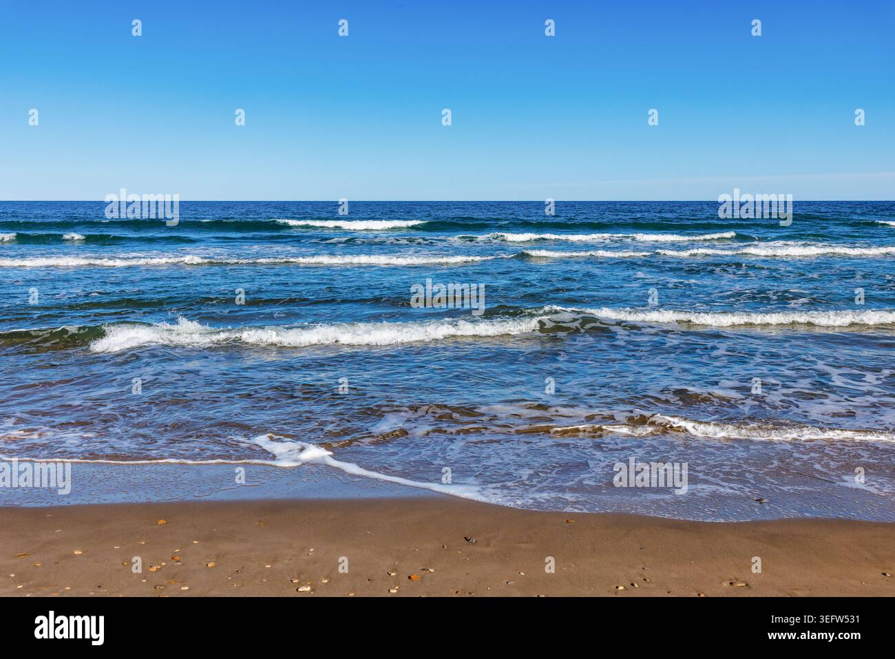 Plage méditerranéenne ensoleillée avec des vagues douces et ciel bleu, paysage côtier de l'Espagne. Banque D'Images