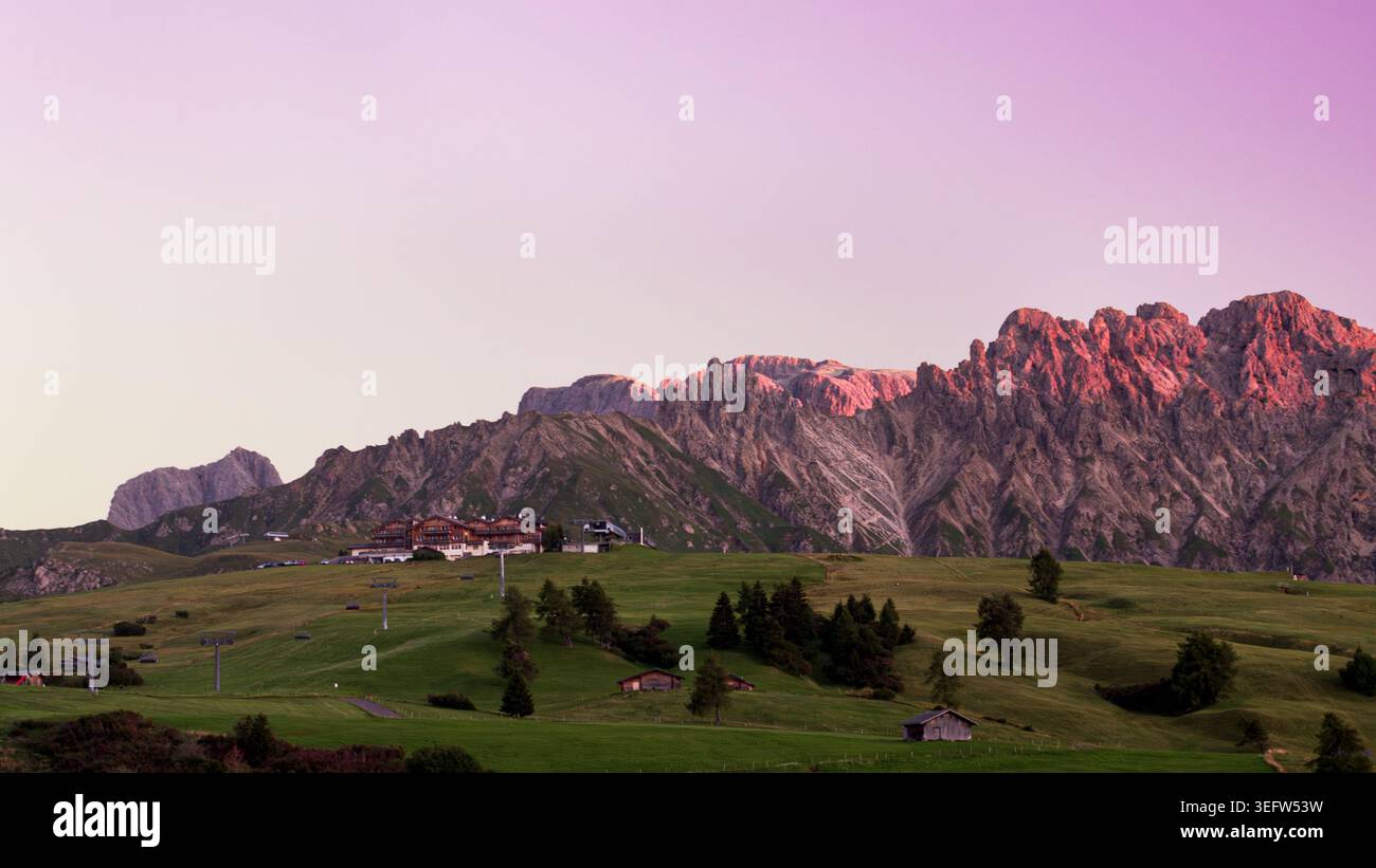 Chaîne de montagnes Dolomites au coucher du soleil avec prairie alpine et chalets Banque D'Images