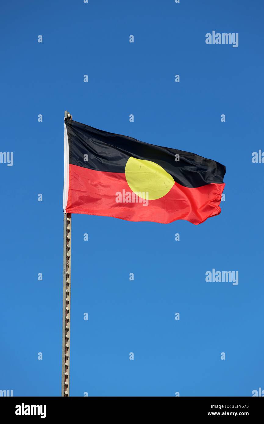 Drapeau aborigène australien agitant sur un mât de drapeau contre un ciel bleu clair Banque D'Images