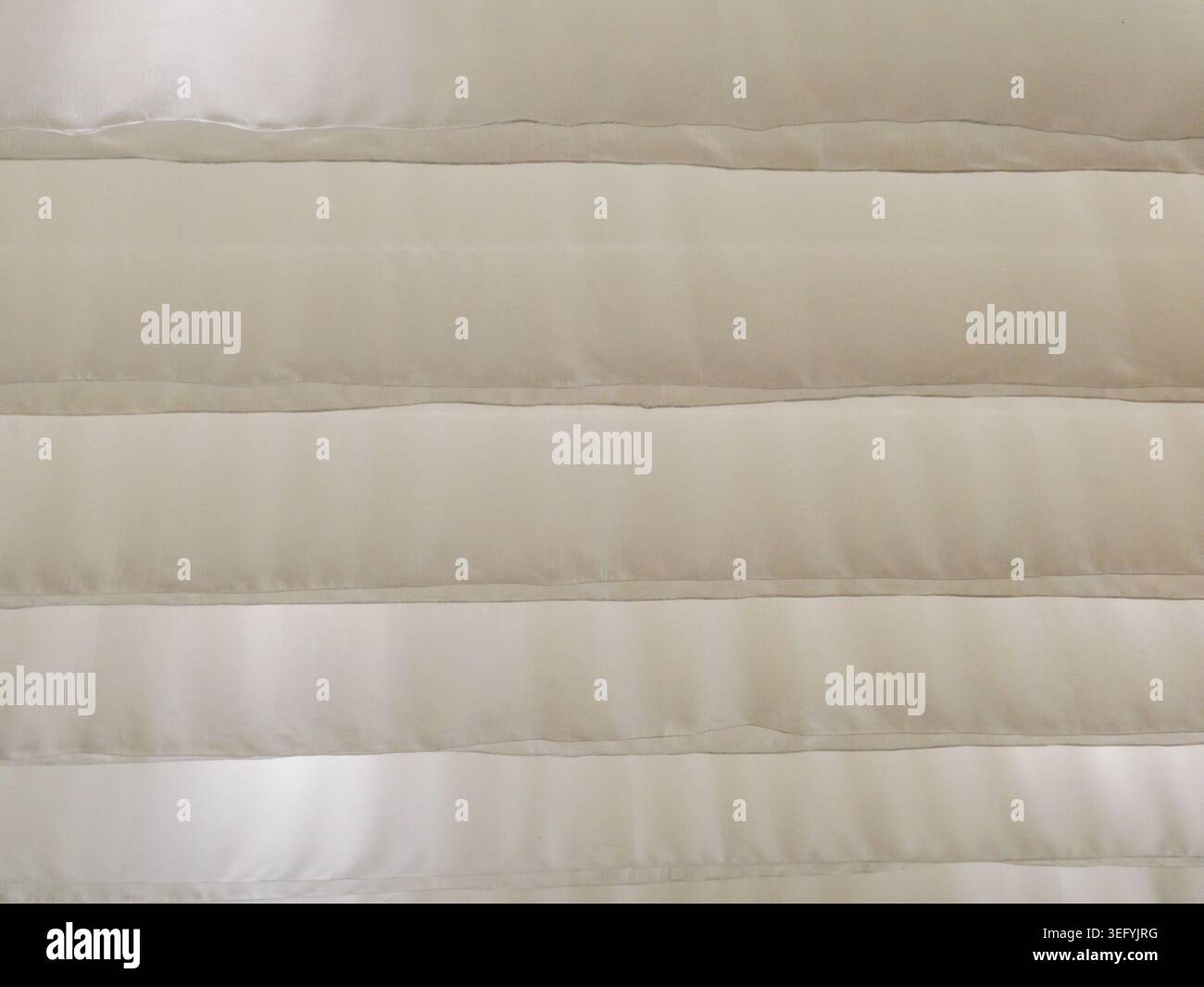 Une vue abstraite en gros plan de stores horizontaux dans un matériau beige texturé. Des étincelles subtiles sont visibles, avec la lumière du soleil filtrant à travers les lattes, c Banque D'Images