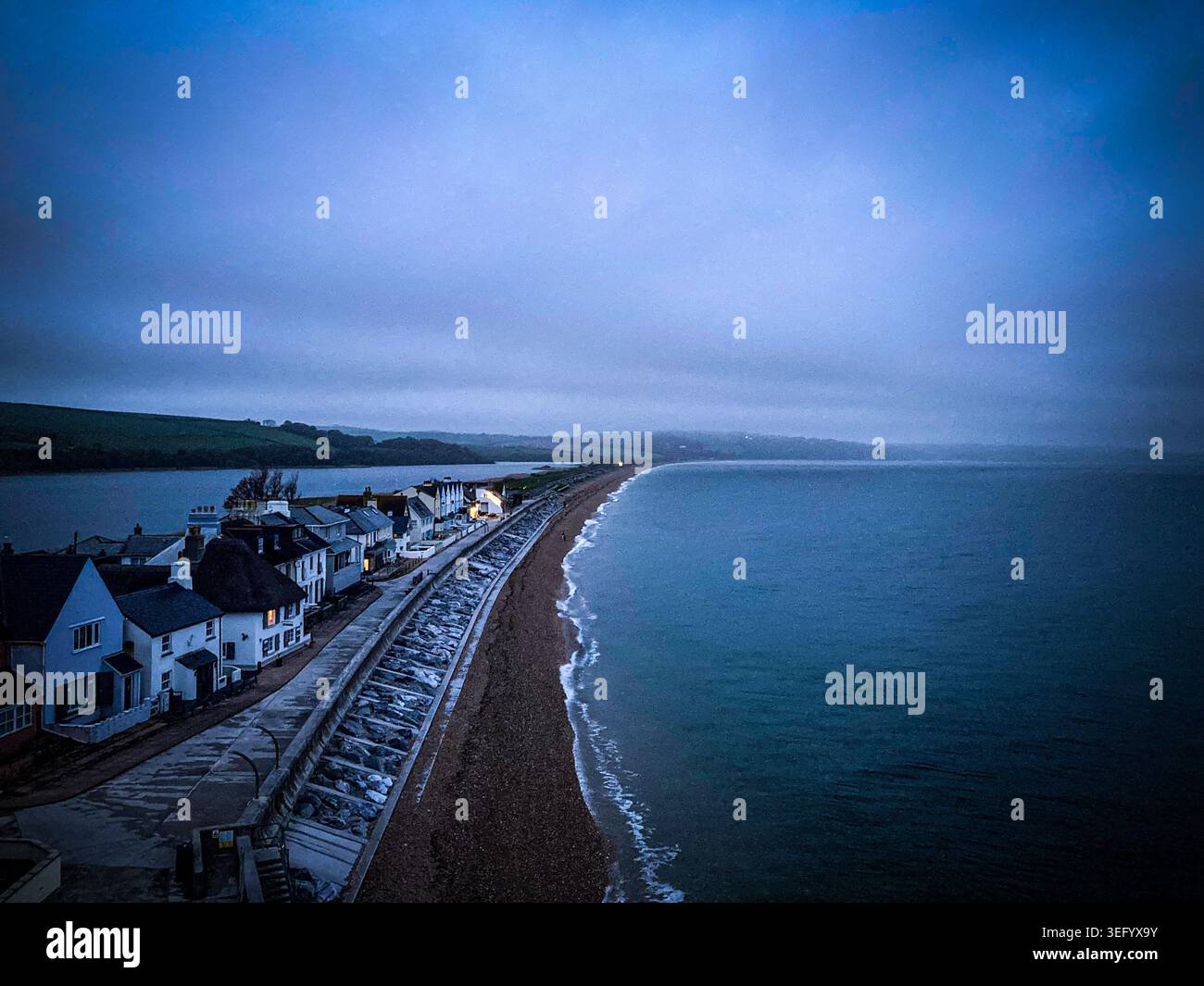 Couchant à Torcross, Slapton Sands, Devon. Une côte déployée avec de petites vagues et des maisons sur la longue plage de galets. - Image de stock capturée avec un smartphone