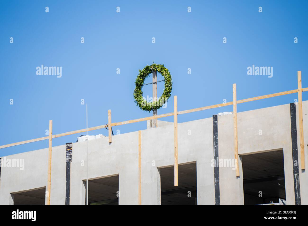Couronne de finition verte traditionnelle sur une traverse en bois célébrant l'achèvement structurel d'un développement de bâtiment moderne en béton armé Banque D'Images