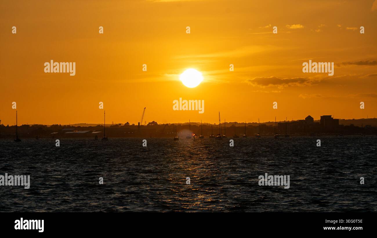 Eaux calmes et coucher de soleil serein sur les bateaux de loisirs à Sandbanks, Poole, Dorset près de Bournemouth avec des surfeurs sur foil naviguant à travers le vent. Banque D'Images