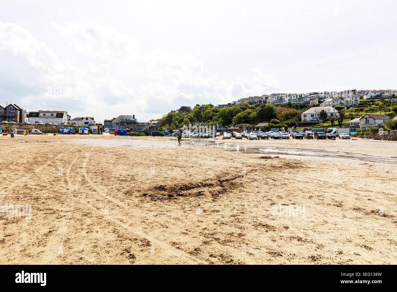 Large plage de sable à Polzeath en Cornouailles avec des traces de pneus et des empreintes visibles sur le sable. Quelques personnes marchent le long du rivage, tandis que les maisons Banque D'Images
