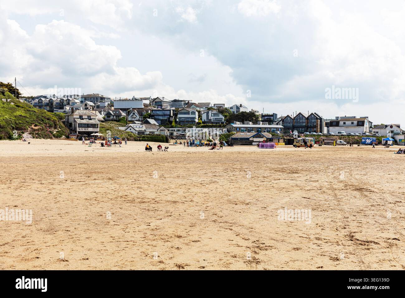 Large plage de sable à Polzeath en Cornouailles avec des traces de pneus et des empreintes visibles sur le sable. Quelques personnes marchent le long du rivage, tandis que les maisons Banque D'Images
