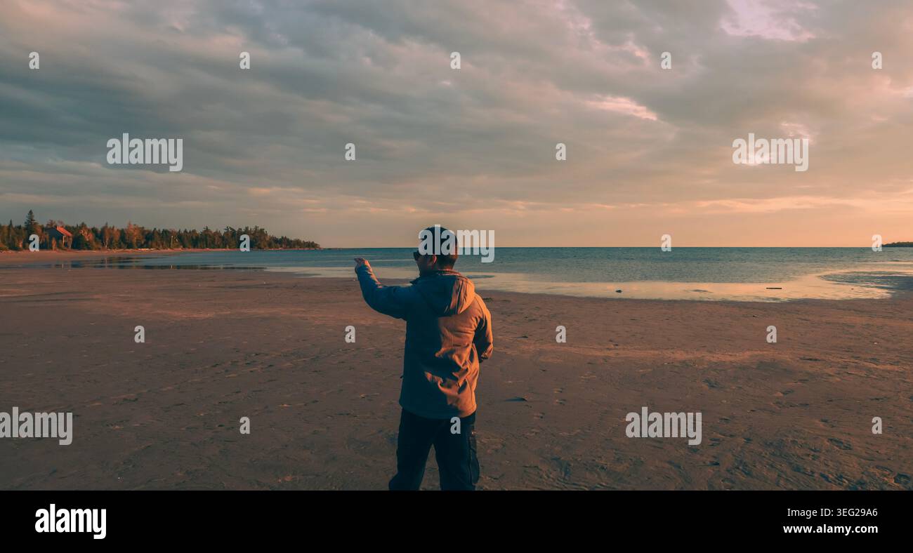 Les gens se tiennent sur le rivage gelé de Singing Sands Beach pendant un coucher de soleil d'hiver éclatant, leurs longues ombres s'étendant sur le sable glacé. Banque D'Images