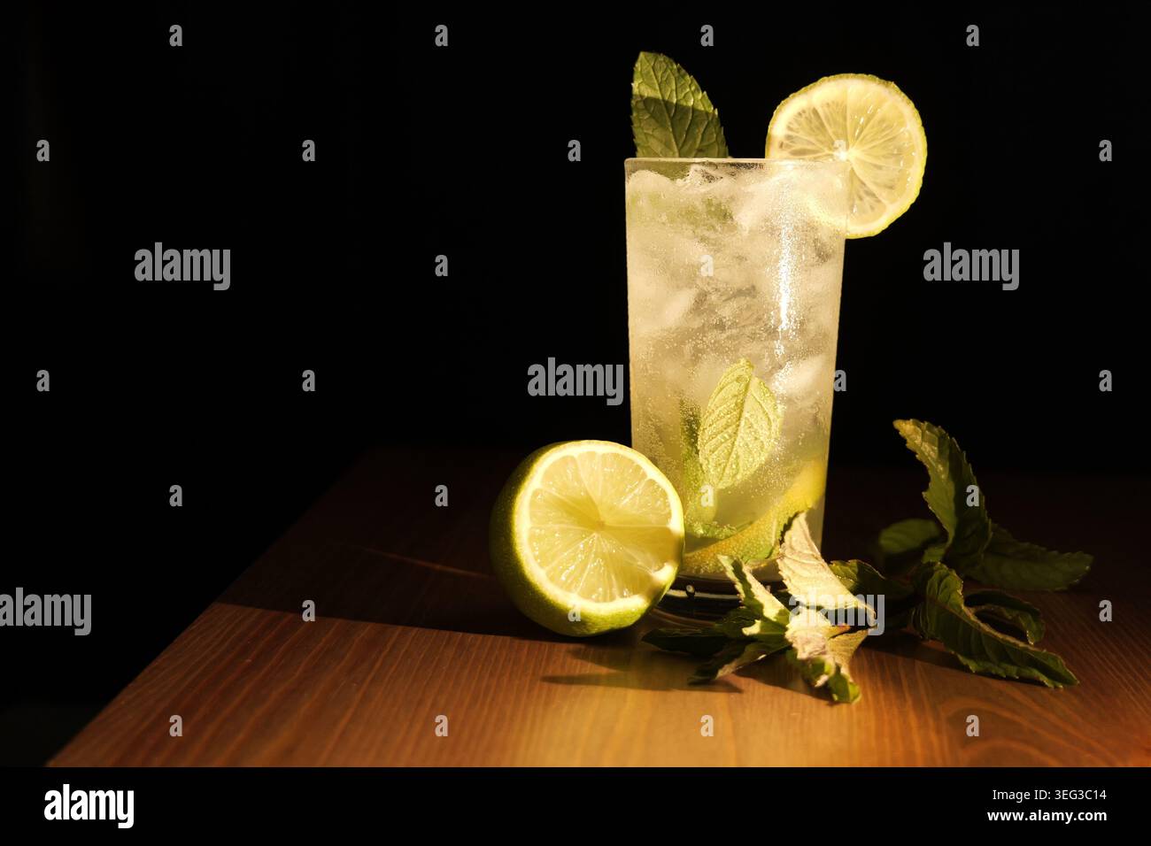 Grand verre de cocktail Mojito classique avec des glaçons, des feuilles de menthe vibrantes et une tranche de citron vert fraîche, reposant sur une surface en bois contre une grotte sombre Banque D'Images