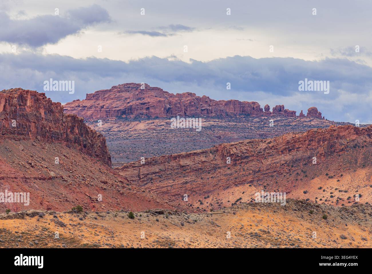 Des falaises de grès rouge érodées et des mesas en couches dominent le paysage désertique aride sous un ciel couvert. Banque D'Images