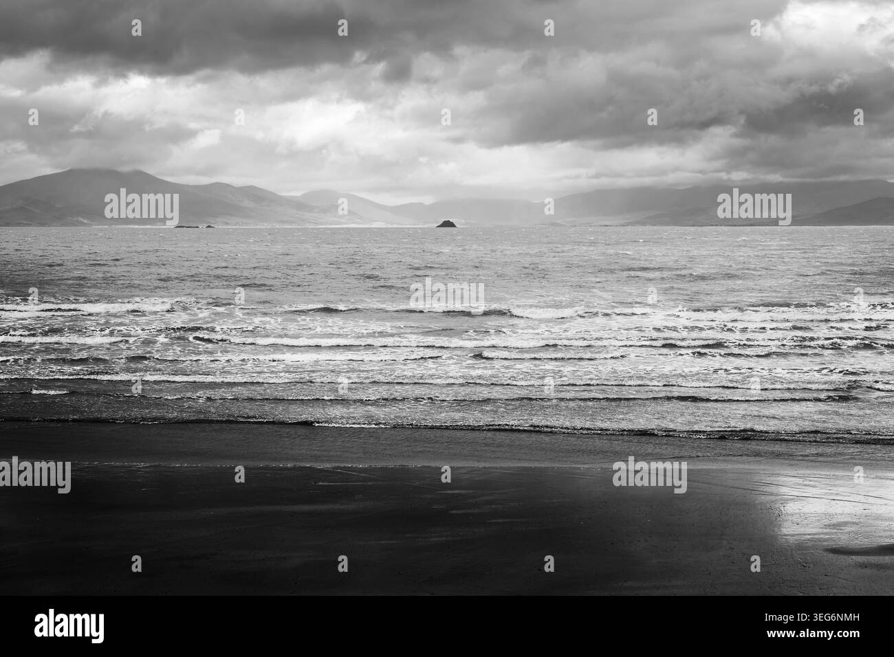 Paysage marin monochrome pittoresque, vagues se brisant sur une plage irlandaise de Kerry avec les montagnes escarpées de la péninsule de Dingle à l'horizon. Banque D'Images