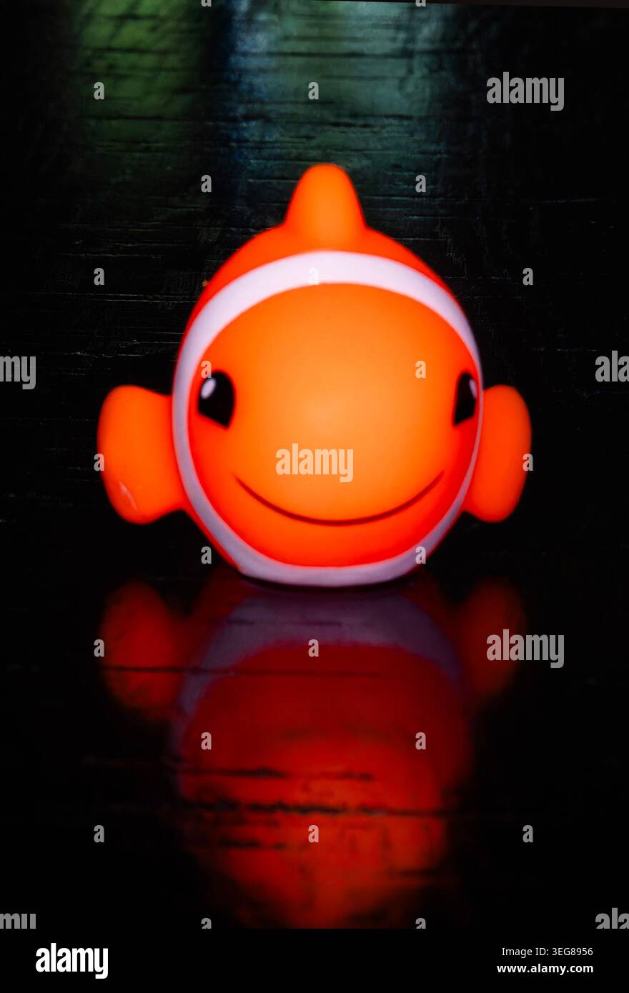 Un mignon jouet poisson clown en bois sur s surface réfléchissante sombre Banque D'Images