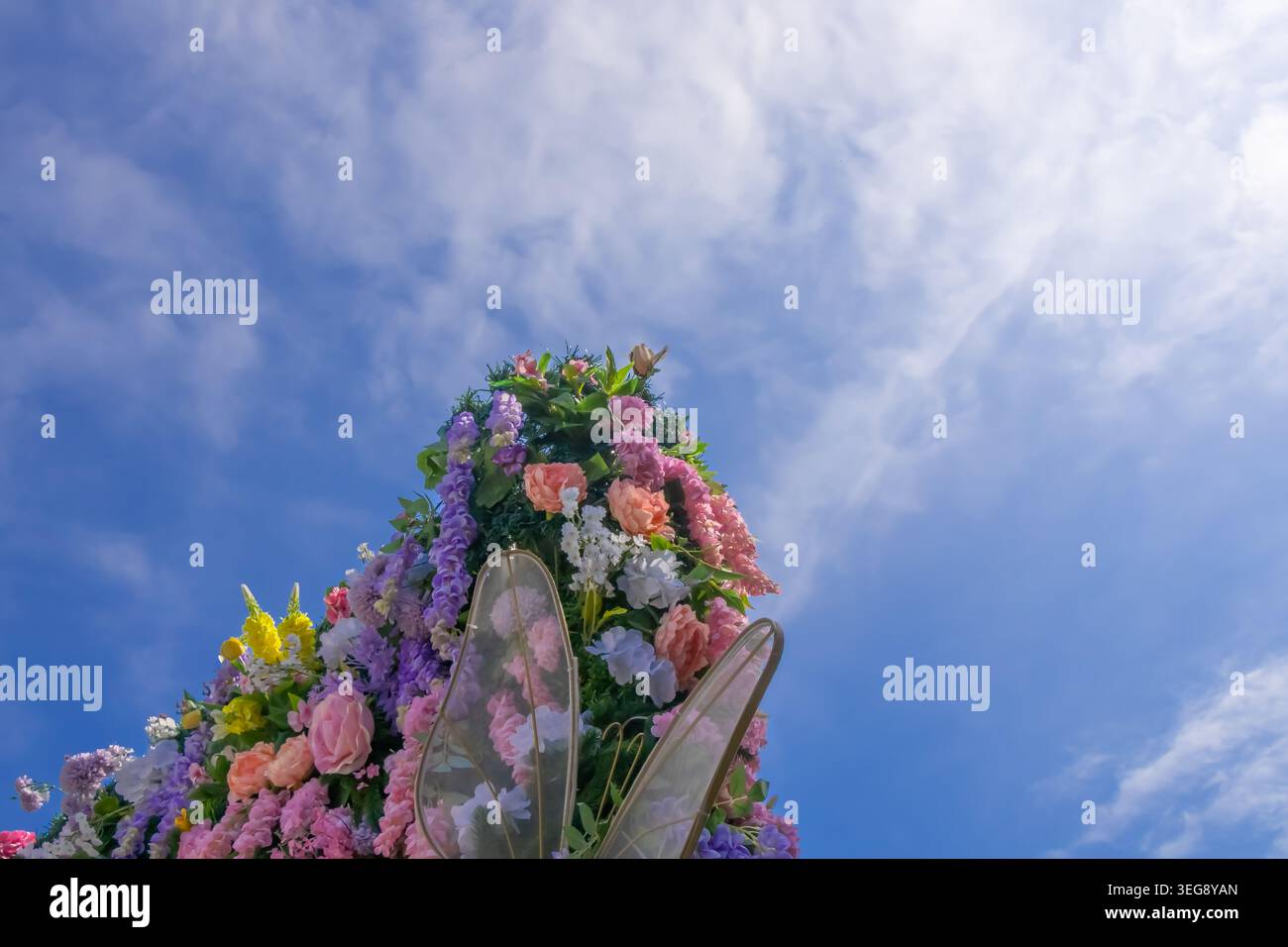 Vue à angle bas de la décoration florale colorée avec des ailes de papillon décoratives sous un ciel bleu vif avec des nuages doux pendant une journée de printemps lumineuse. Banque D'Images