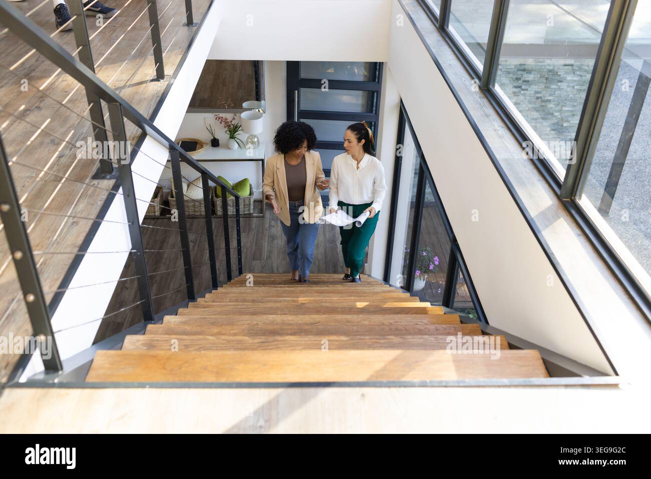 Deux femmes adultes montant des escaliers en bois dans un grenier, portant des blazers et tenant des documents roulés Banque D'Images
