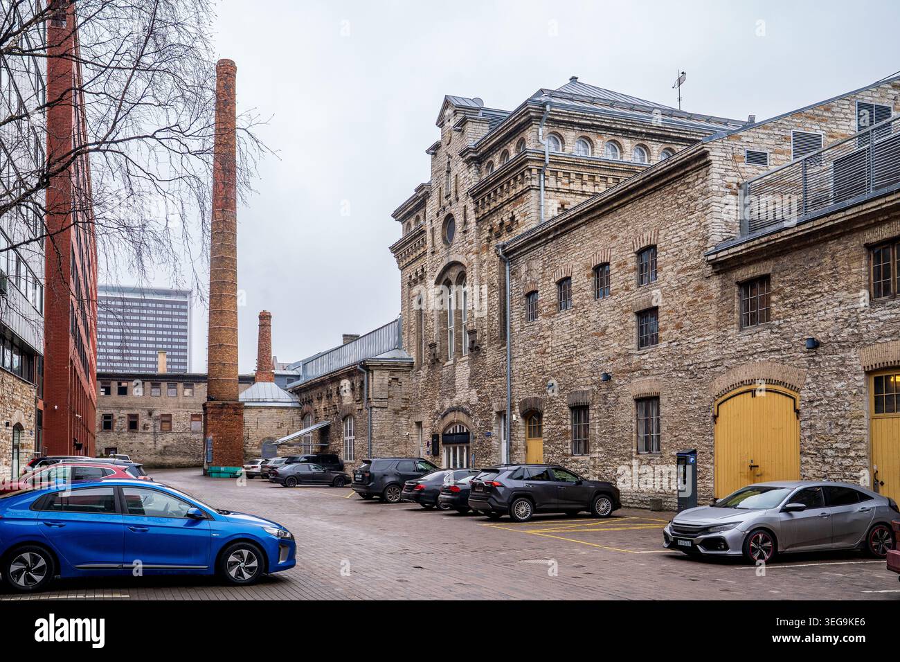 Un parking situé parmi les bâtiments historiques en calcaire du quartier Rotermann à Tallinn, Estonie. La scène présente des cheminées industrielles imposantes Banque D'Images