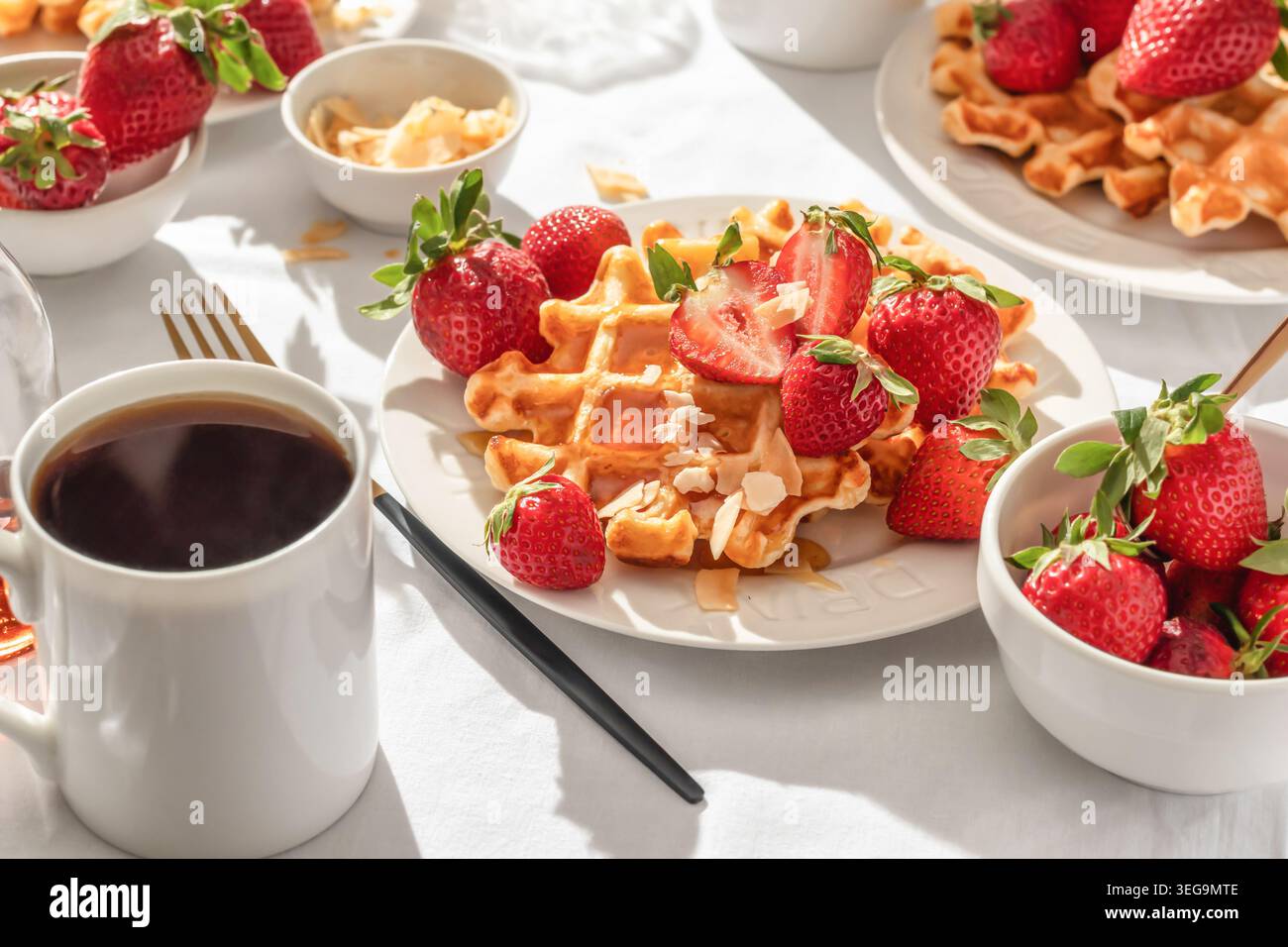 Gaufres belges avec fraises fraîches et miel sur plaque blanche sur fond de nappe blanche. Petit déjeuner d'été sucré dans la lumière du matin ensoleillée et lumineuse Banque D'Images