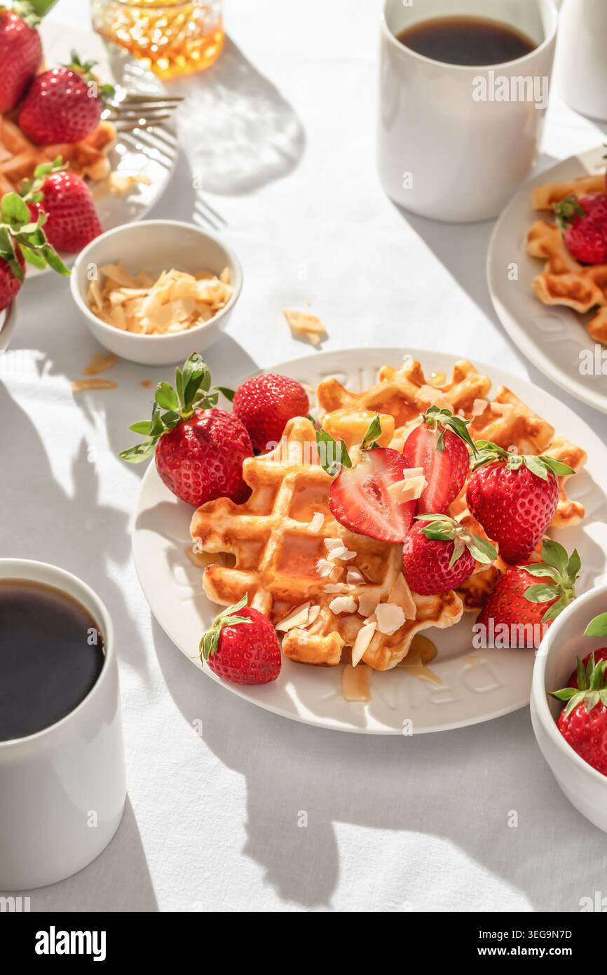 Gaufres belges avec fraises fraîches et miel sur plaque blanche sur fond de nappe blanche. Petit déjeuner d'été sucré dans la lumière du matin ensoleillée et lumineuse Banque D'Images