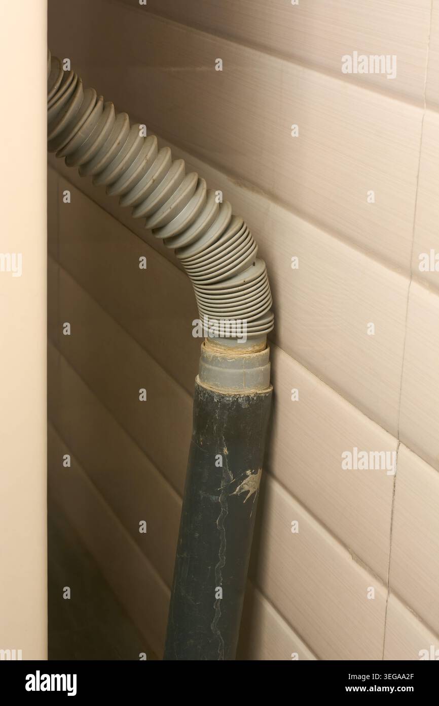 tuyau d'évacuation en plastique flexible ondulé gris sale connecté à un tuyau en pvc rigide, installation de plomberie verticale, vue rapprochée sur fond de mur carrelé Banque D'Images