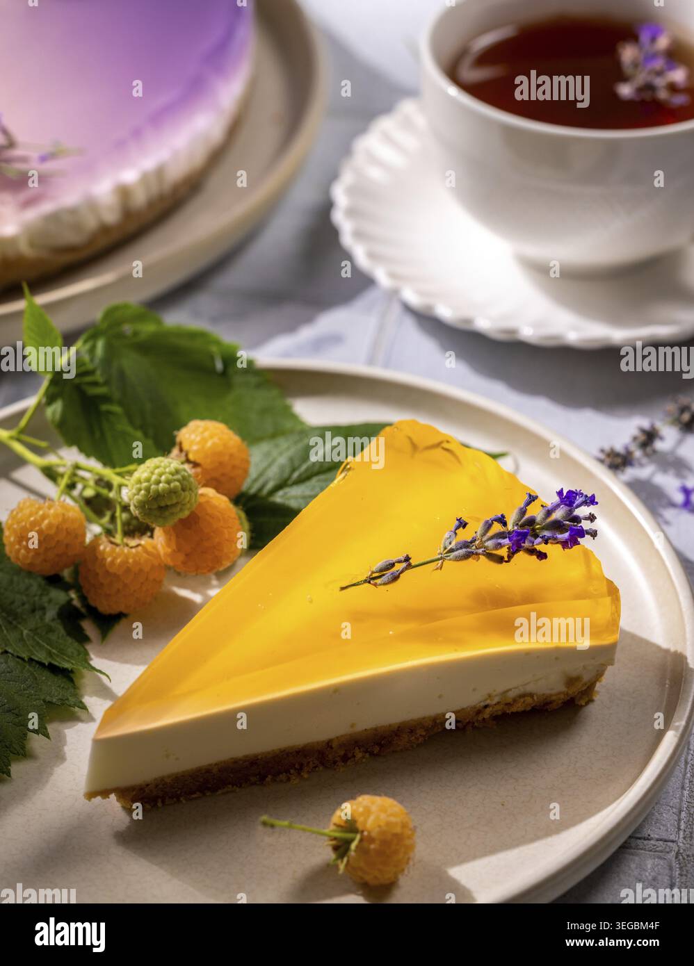 Tranche de cheesecake crémeuse avec garniture de gelée vive, garnie d'une branche de lavande, servie avec des framboises jaunes fraîches et du thé Banque D'Images