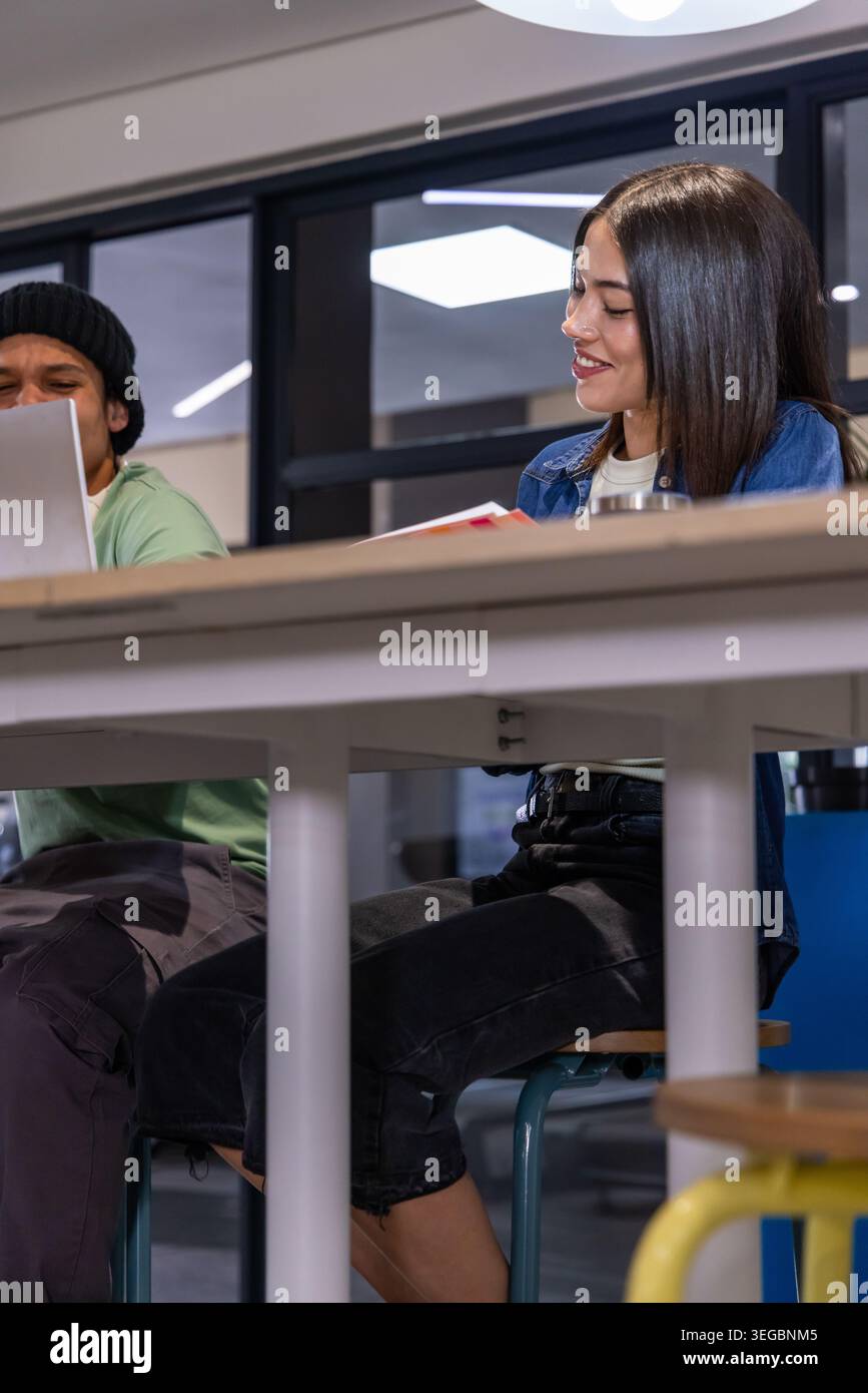 Divers collègues assis à une grande table commune dans un espace de travail moderne, en utilisant un ordinateur portable et un ordinateur portable Banque D'Images