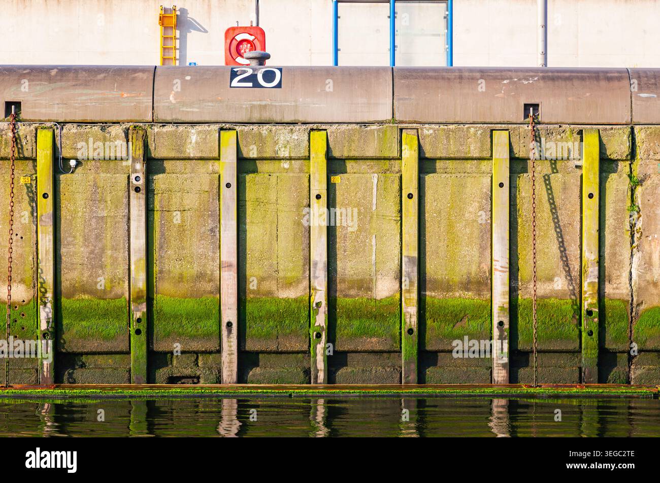 Mur de quai portuaire en béton avec des algues de mousse verte et des chaînes rouillées au niveau de la mer dans un terminal portuaire Banque D'Images