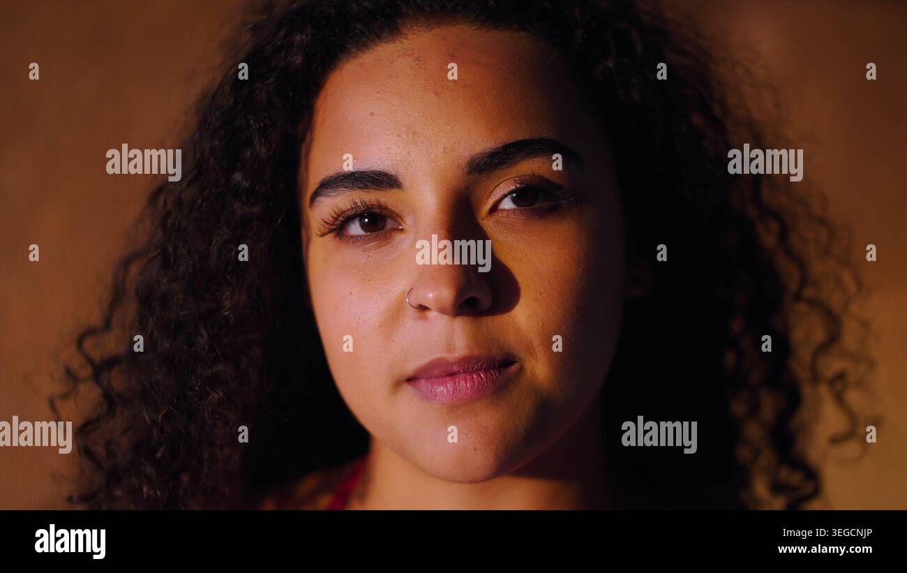 Jeune femme avec des cheveux bouclés naturels et anneau de nez regardant directement le spectateur Banque D'Images