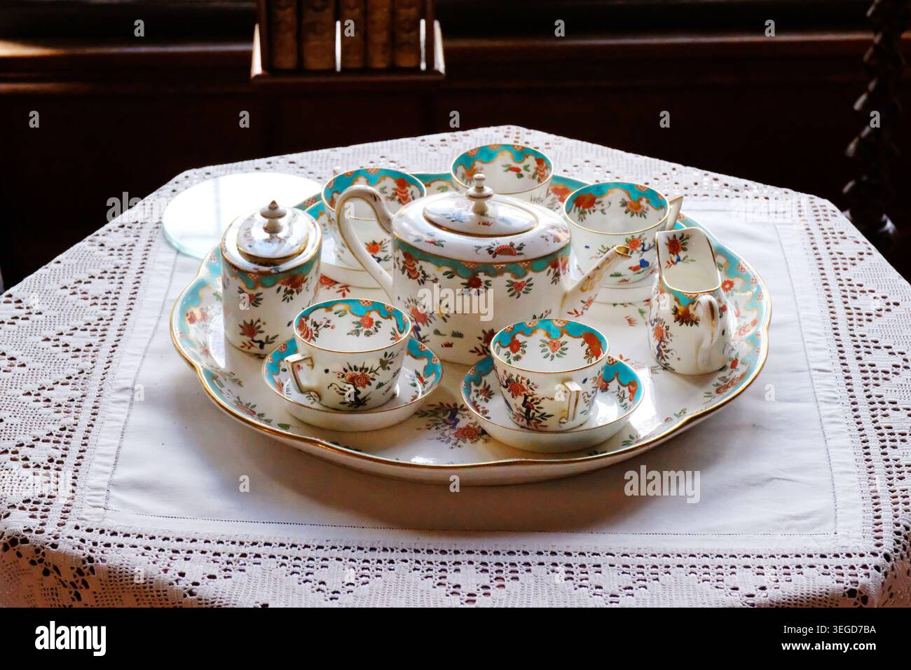 Gros plan détaillé d'un service à thé en porcelaine antique disposé sur un plateau de service assorti reposant sur une nappe blanche en dentelle au crochet. Banque D'Images