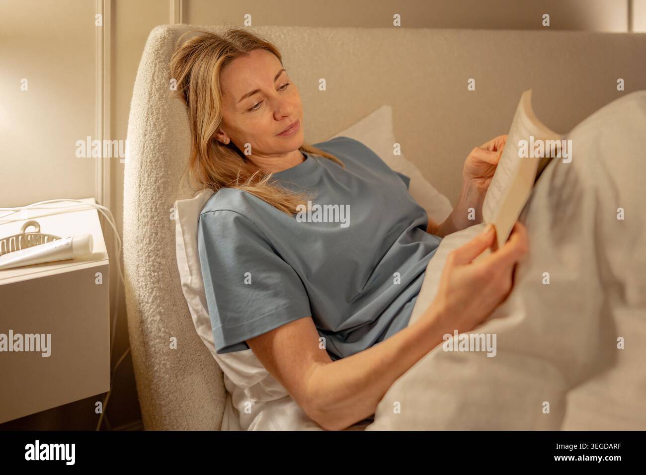 Femme allongée dans le lit, lisant le livre pendant la soirée tranquille à la maison. Routine de coucher calme, relaxation, slow living, concept de détox numérique. Paisible femme e Banque D'Images