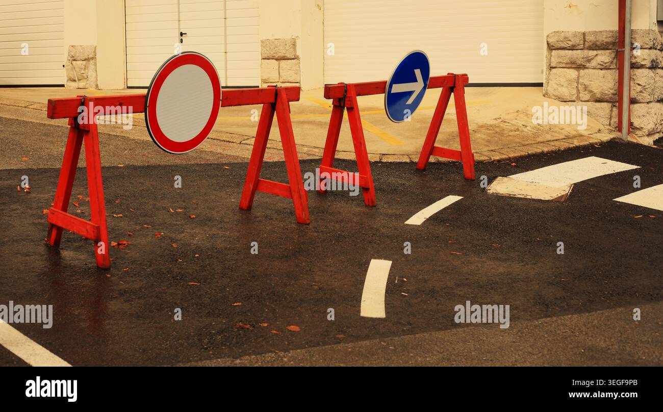 Des panneaux de signalisation routière temporaires fermés et des barrières d'avertissement rouges et blanches bloquant une rue asphaltée pendant les travaux routiers. Banque D'Images