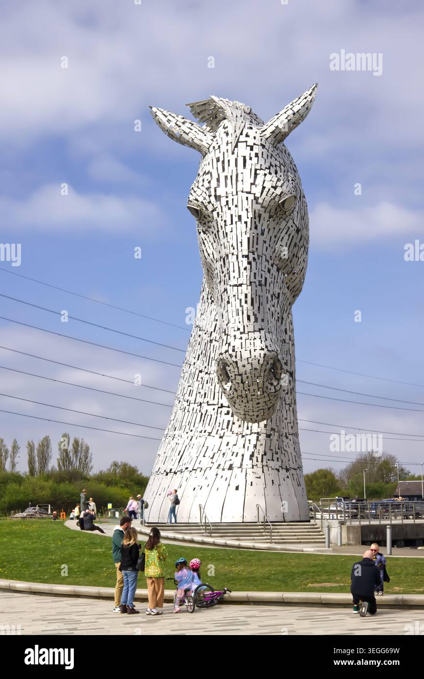 Une jeune famille visitant les Kelpies à Falkirk, en Écosse, sous l'une des sculptures géantes de tête de cheval par une journée ensoleillée. Banque D'Images