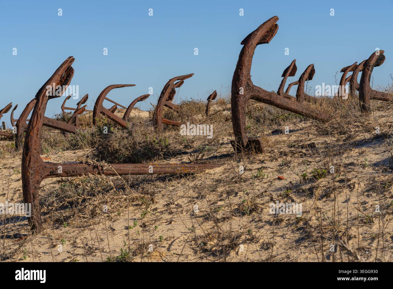 Une ancre en décomposition dépasse du sable au milieu d'une végétation côtière clairsemée sur Praia do Barril. Banque D'Images