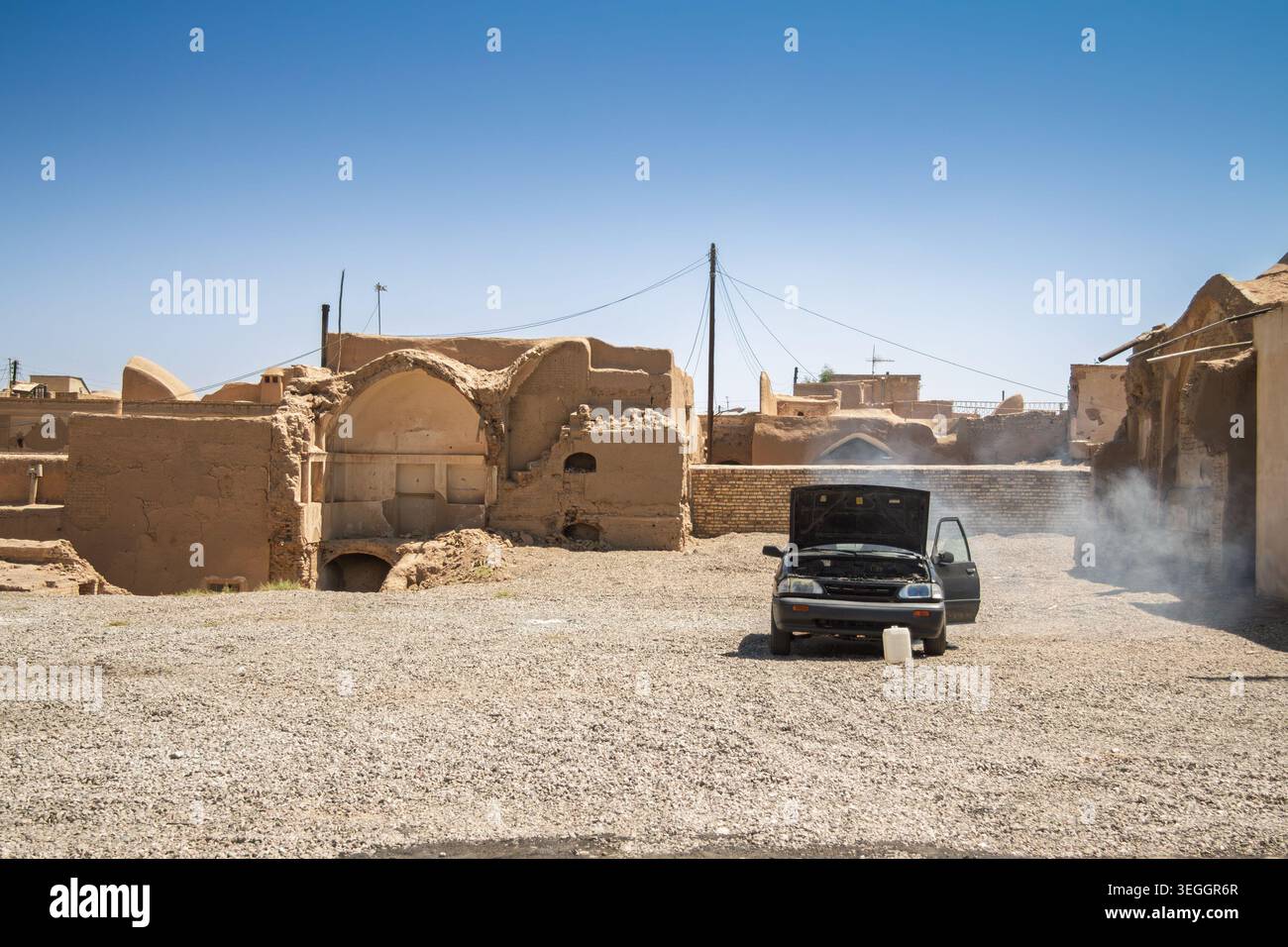 Voiture surchauffée avec capot ouvert et vapeur montante à Kashan, Iran, montrant des réparations sur le bord de la route dans un vieux quartier de la ville pendant les températures brûlantes de l'été A. Banque D'Images
