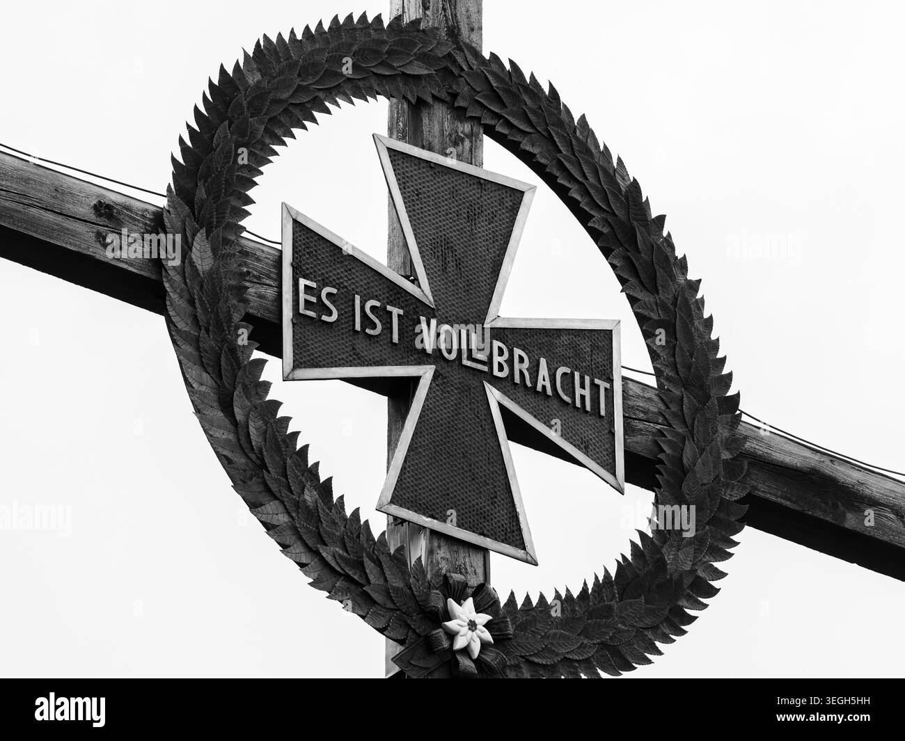 Winklern, Autriche - 16 juillet 2021 : Croix de fer avec couronne de feuilles de chêne sculptées et plaque en étain es ist Vollbracht accompagnée d'un stand de fleurs edelweiss Banque D'Images