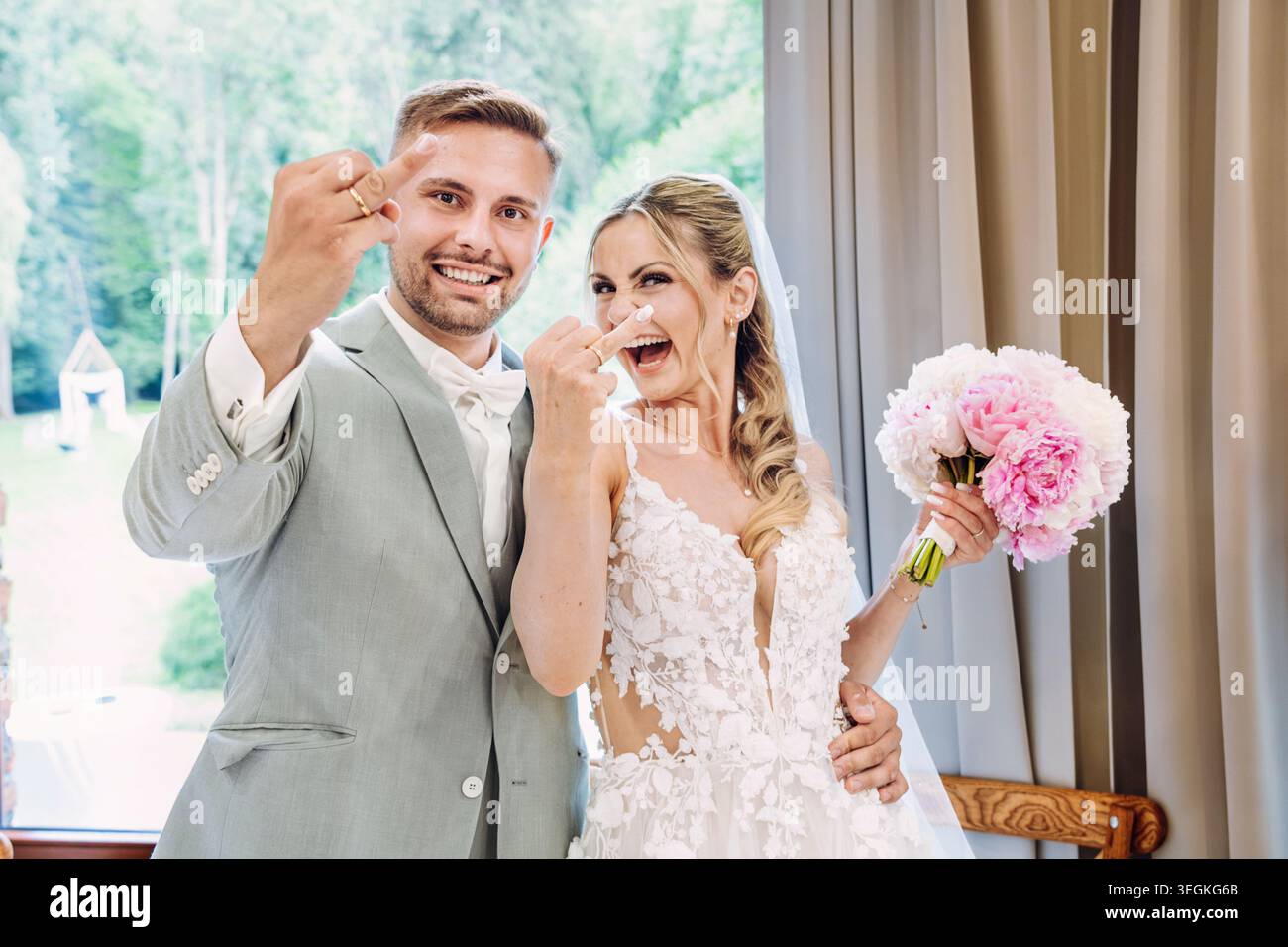 mariée et mariée joyeuse et riante au mariage. Mariée et mariée montrent gaiement les bagues sur leur majeur ou annulaire à la caméra. Banque D'Images
