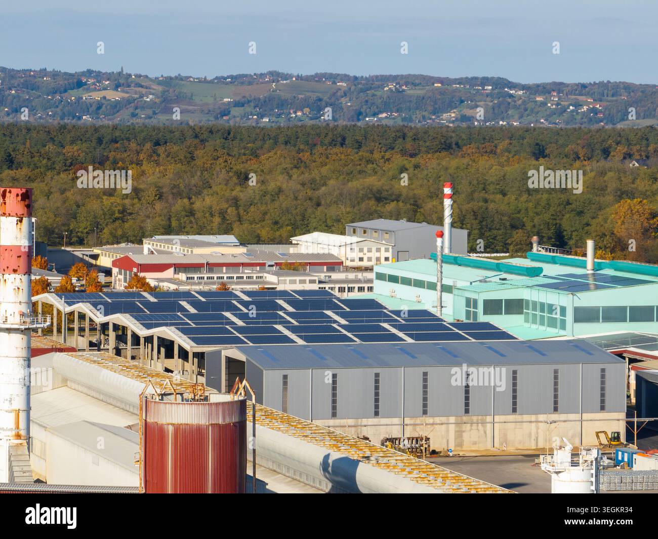 La vue aérienne capture un site industriel avec des bâtiments et des panneaux solaires entourés d'arbres et de champs par temps clair. Banque D'Images