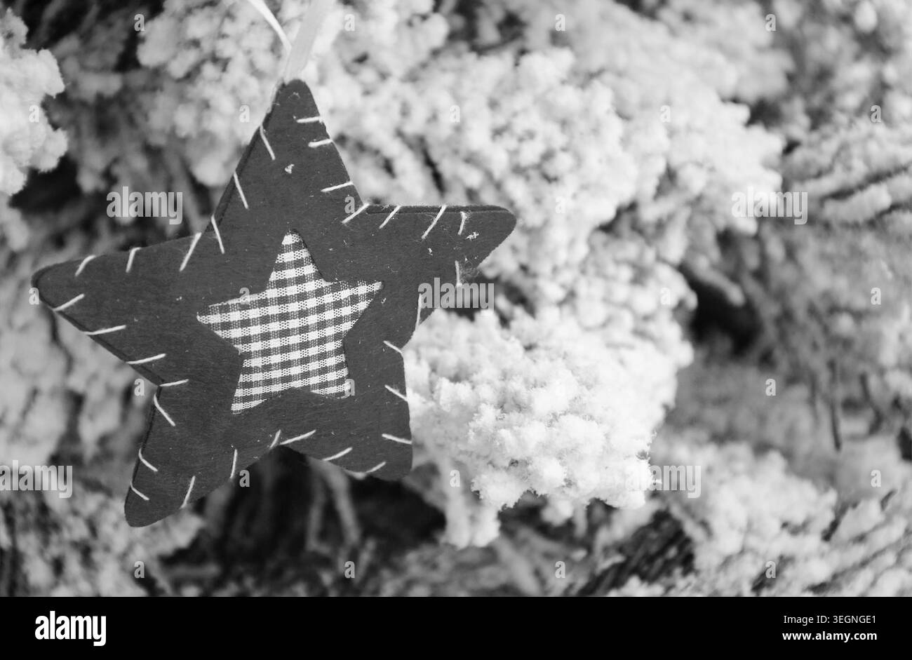 Ornement d'étoile textile fait à la main accroché sur l'arbre de Noël couvert de neige, fond de vacances d'hiver vintage confortable, photo historique noir et blanc Banque D'Images