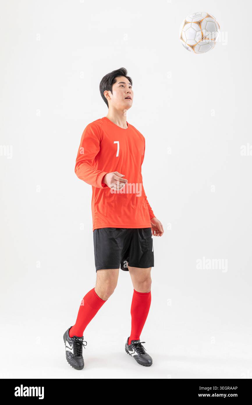 Un jeune homme asiatique en maillot de football, attrapant un ballon de football dans les airs. Banque D'Images