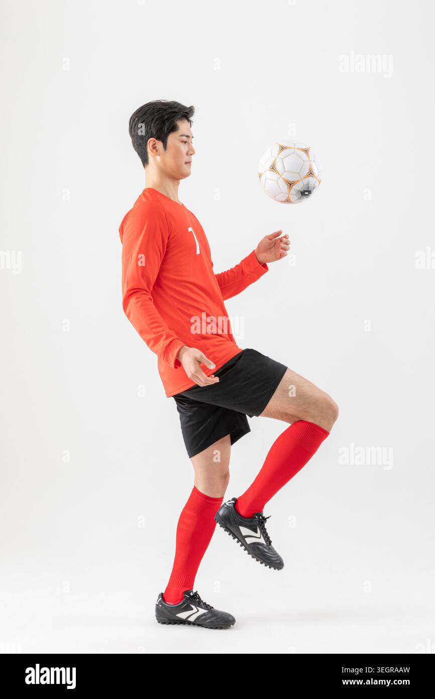 Un jeune asiatique portant un maillot rouge et un short noir jongle avec un ballon de football avec son pied gauche. Banque D'Images