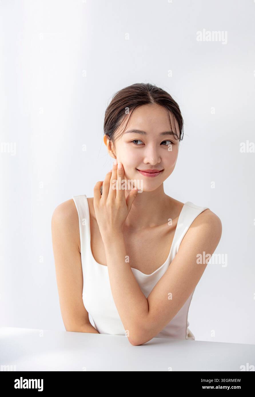 Une jeune femme asiatique la main sur la joue, souriante et regardant directement la caméra. Banque D'Images