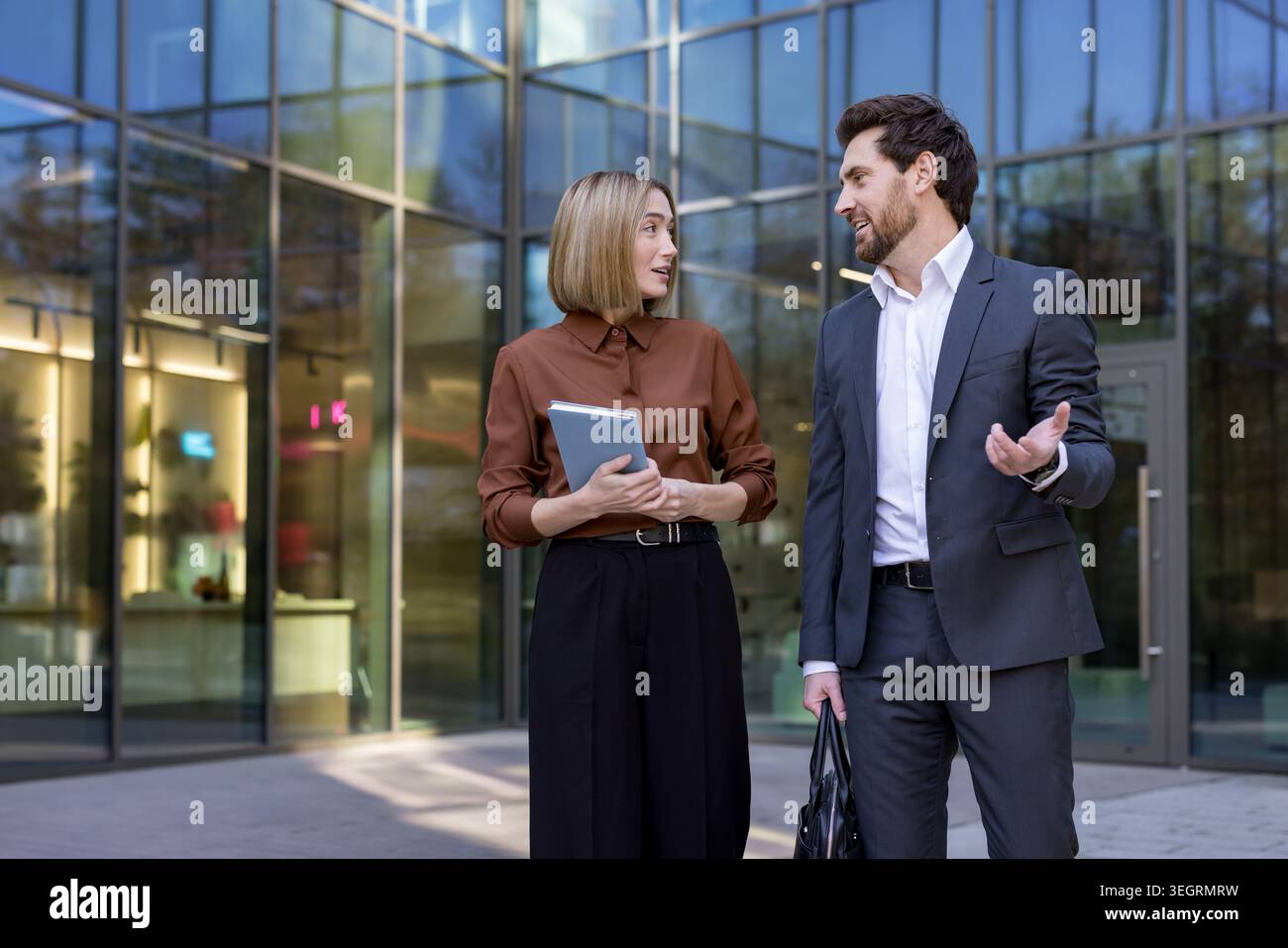 Deux collègues professionnels ont une discussion importante tout en se tenant à l'extérieur d'un immeuble de bureaux moderne, partageant des idées et collaborati Banque D'Images