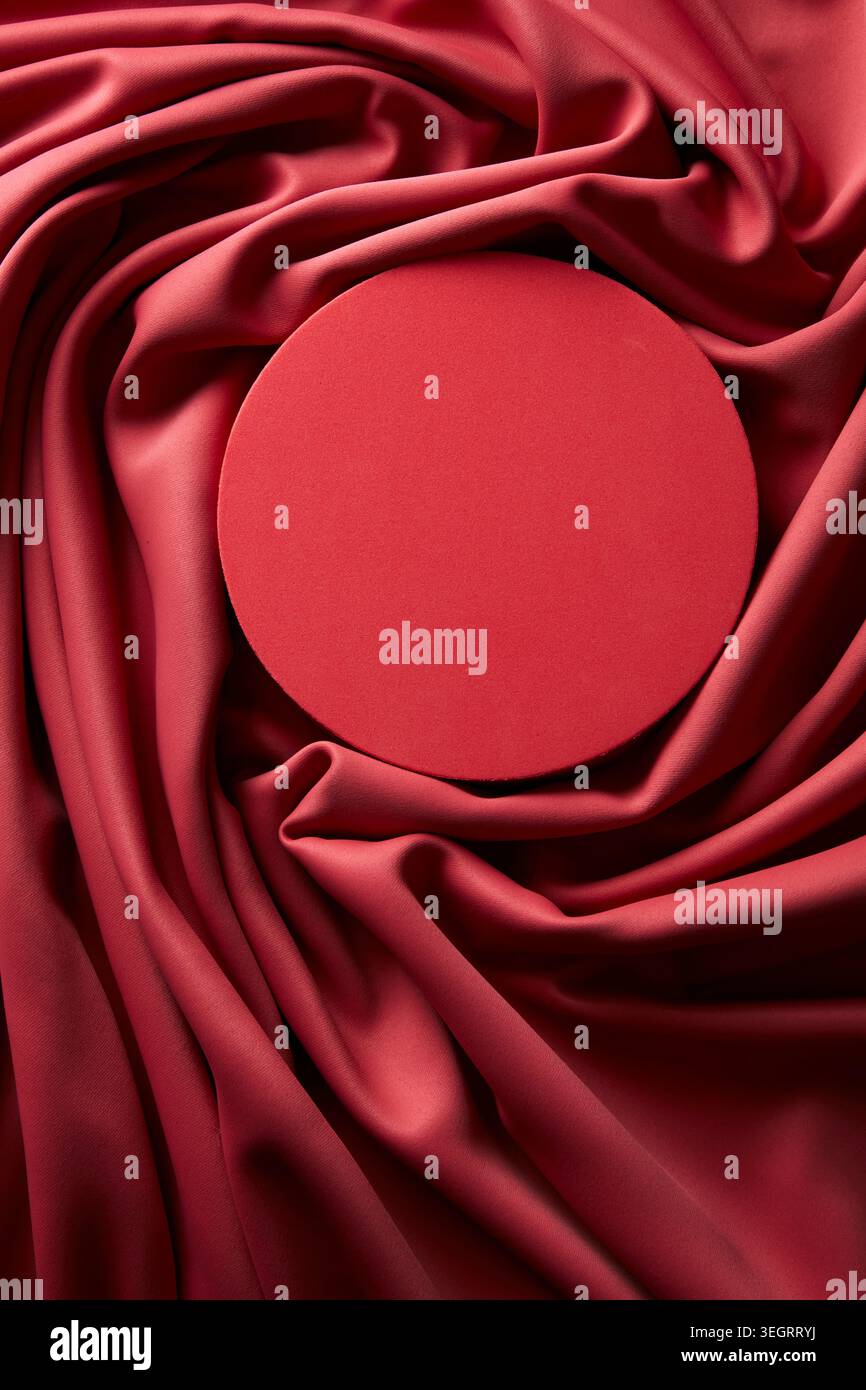 Un objet circulaire rouge est placé sur un tissu rouge, créant une composition simple et directe. Banque D'Images